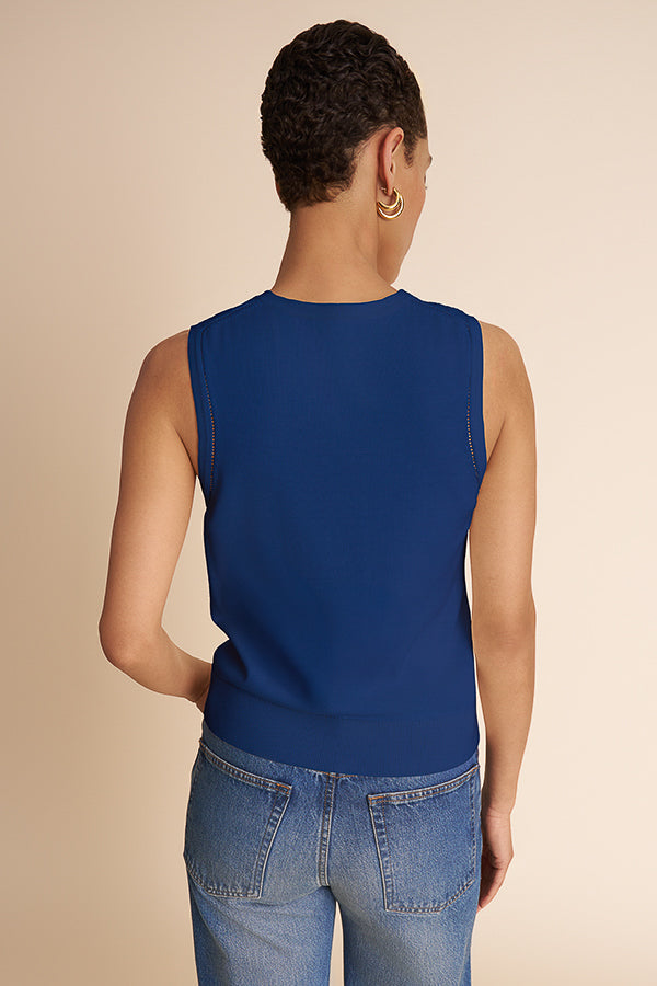 Person wearing a blue sleeveless top and jeans on a beige background | Exclude | Grid Hover