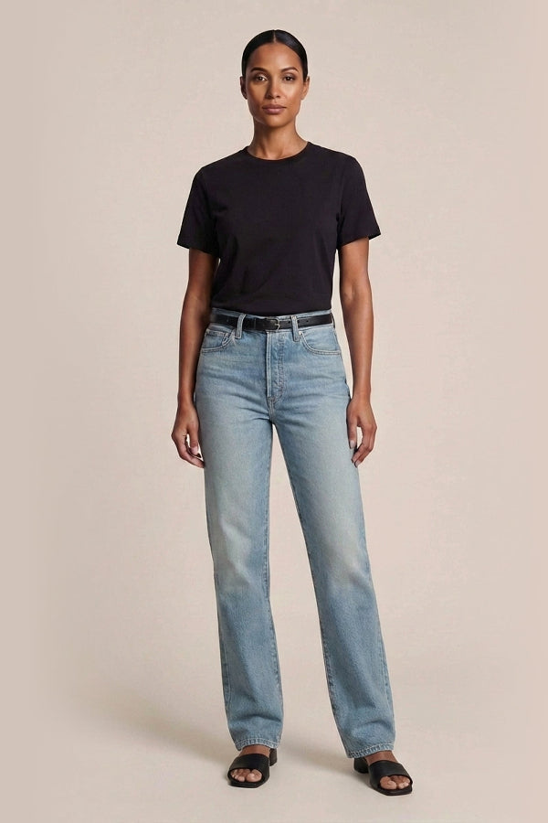 Woman wearing a black t-shirt and light blue jeans on a beige background. | Exclude