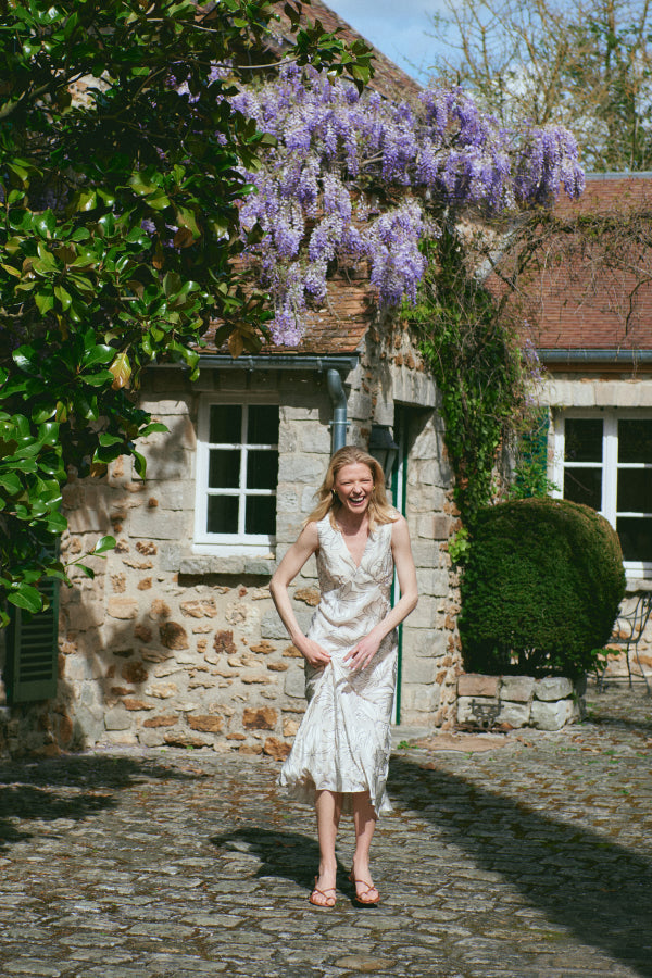 Woman in a white dress standing in front of a stone building with wisteria | Exclude