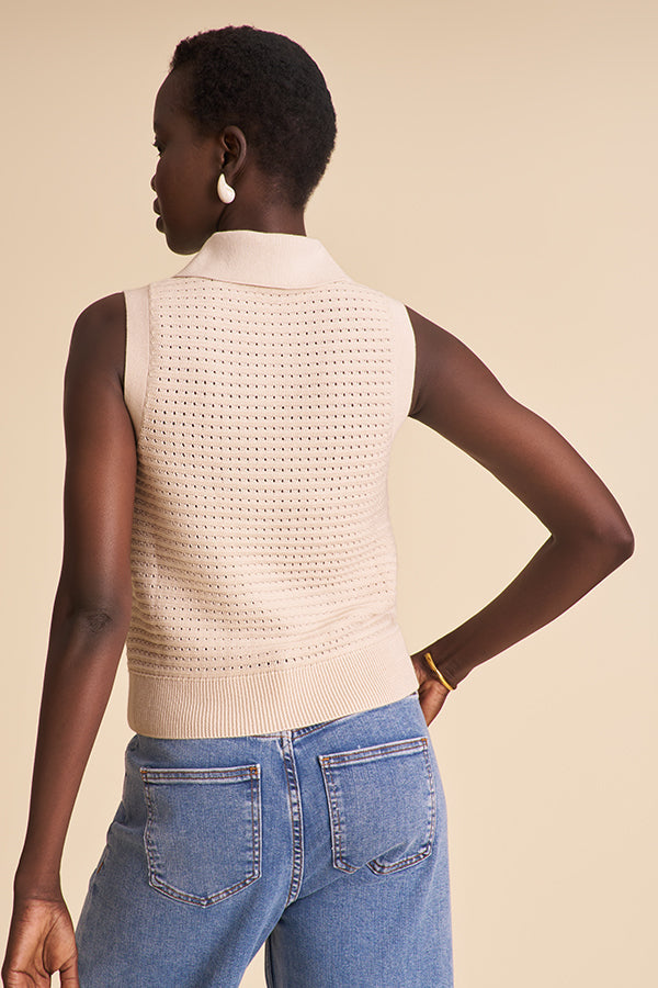 Person wearing a beige knitted vest and blue jeans on a beige background | Exclude