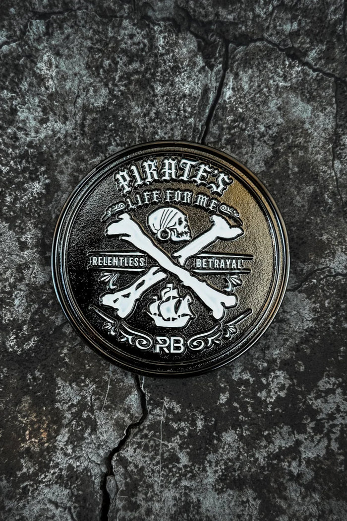A handcrafted round emblem on a cracked, rocky surface features a pirate skull, crossbones with an anchor, and the text Pirates, Life for Me. It celebrates Relentless Adventure and displays initials PB, representing the Pirates Life Challenge Coin by Relentless Betrayal.