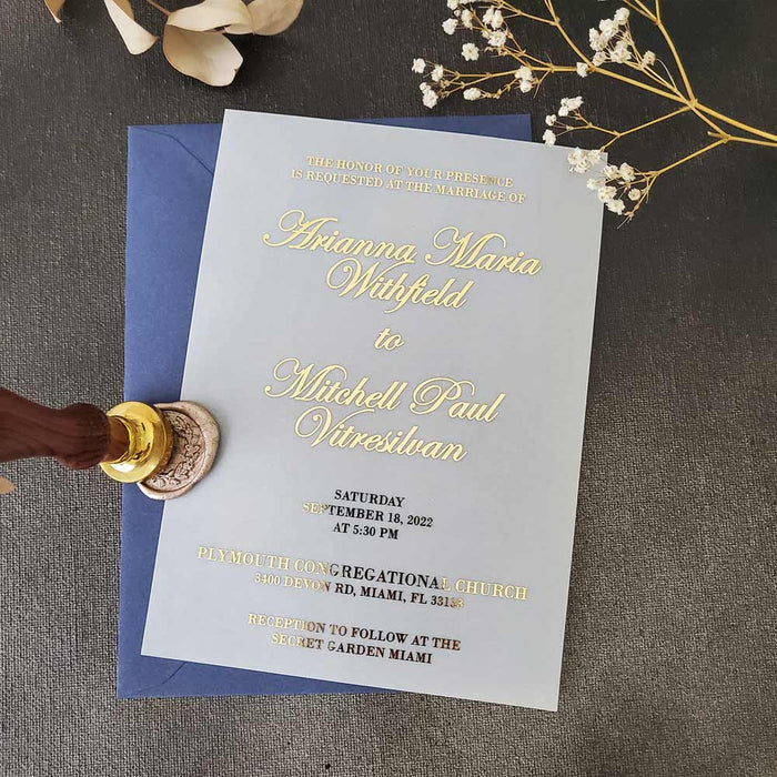 vellum wedding invitation printed in luxurious gold foil lettering, standing upright among soft dried flowers and warm light, highlighting its delicate transparency and elegant typography – XOXOKristen