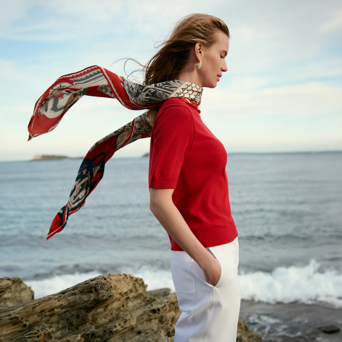 Woman with a patterned scarf standing on a rocky beach with ocean in the background