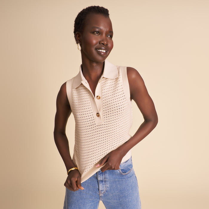 Woman wearing a beige sleeveless top with buttons and blue jeans on a beige background | Lead