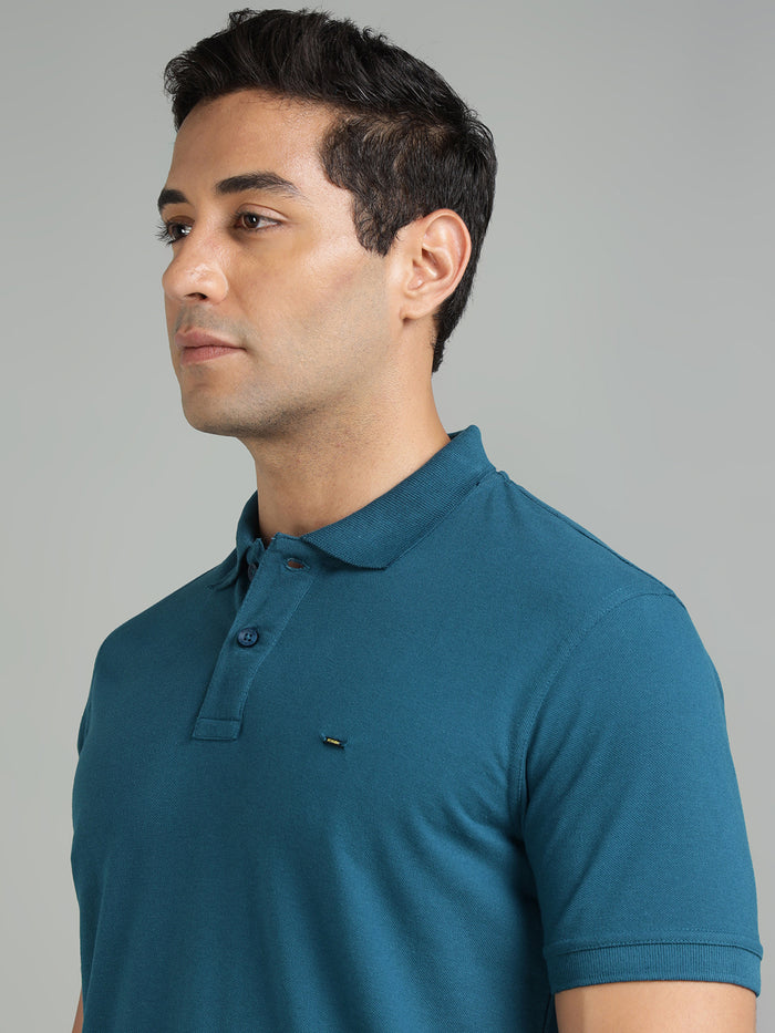 Man wearing a teal polo shirt against a gray background
