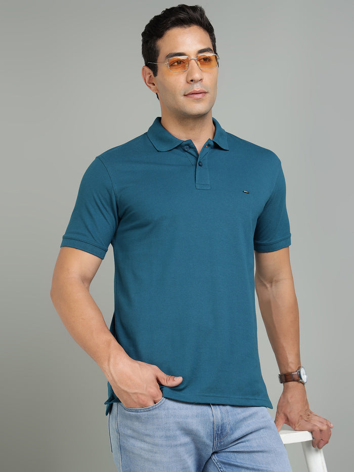Man wearing a teal polo shirt and sunglasses against a gray background