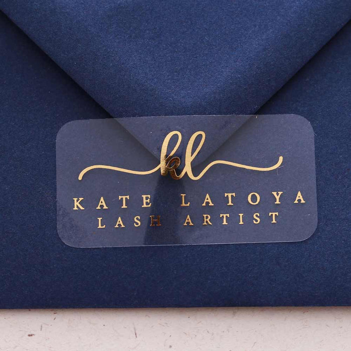 Custom personalized clear glossy rectangular business branding sticker with curly monograms and serif info text in gold foil print sealing navy blue envelope - XOXOKristen