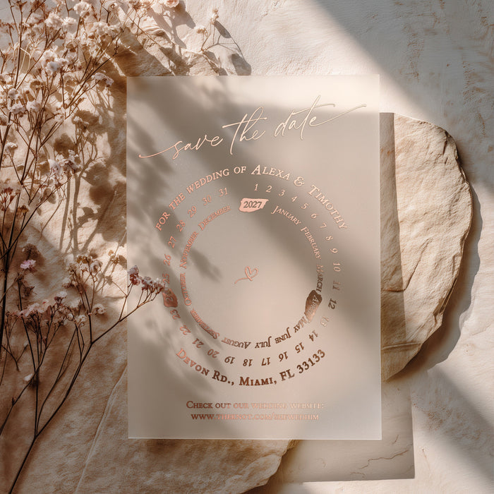 Transparent vellum Save the Date card with rose-gold foil accents and circular layout, styled on warm stone background with dried florals – XOXOKristen