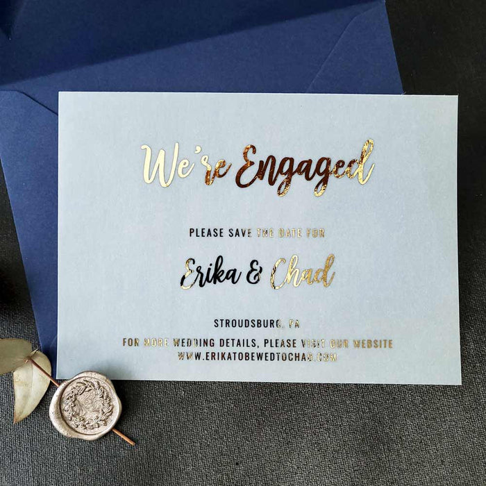 A gold foil vellum Save the Date card placed among dried flowers and soft shadows. The natural lighting highlights the transparent material, creating a dreamy, romantic atmosphere perfect for luxury wedding stationery - XOXOKristen