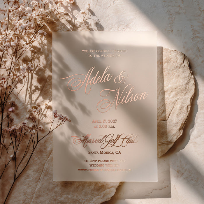 Frosted vellum wedding invitation featuring rose-gold foil print, romantic typography, and RSVP website line, styled on warm stone with floral accents – XOXOKristen